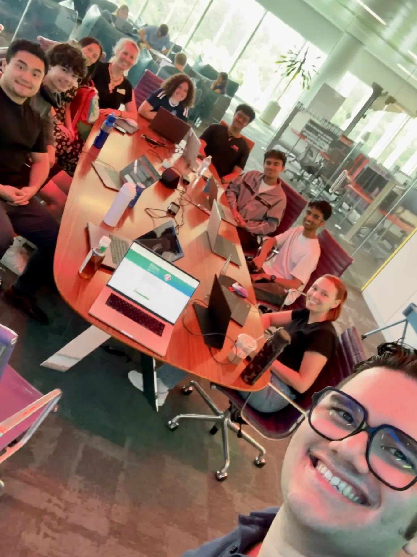 A selfie of teachers and developers smiling around a conference table covered with laptops.