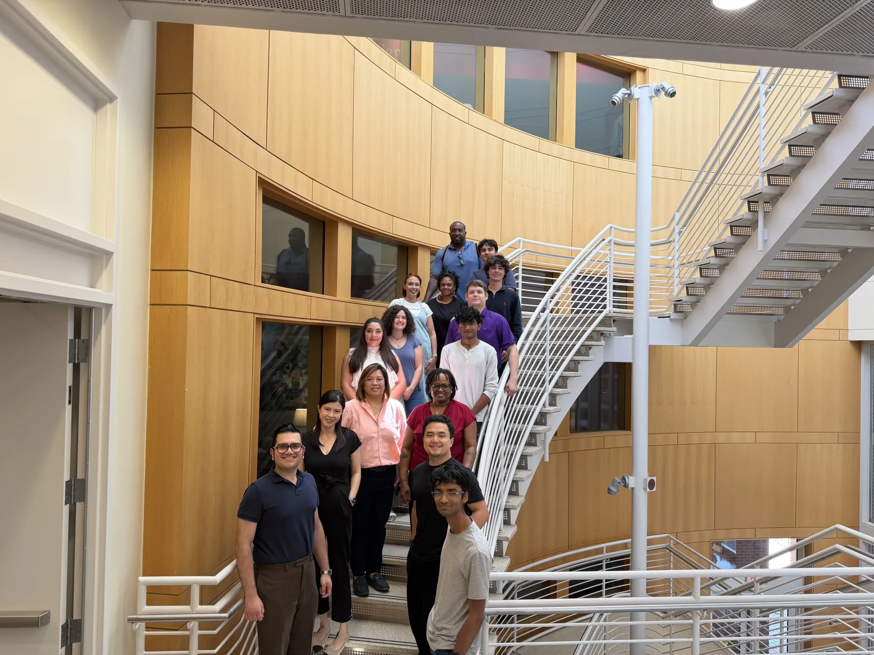 About twenty ExLAIM participants posing on a curved staircase in a university building.